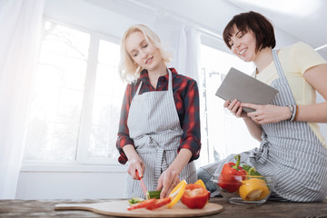 Tasty salad. Nice pleasant young woman standing in the kitchen and cutting cucumber while preparing a salad