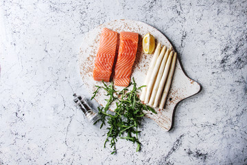 Sliced raw uncooked salmon fillet on wooden chopping board as fish shape with ingredients for...
