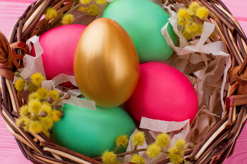 Close up colorful Easter eggs in basket. Colorful eggs and golden egg decorated with pussy-willow branches in woven basket. Happy Easter holiday.