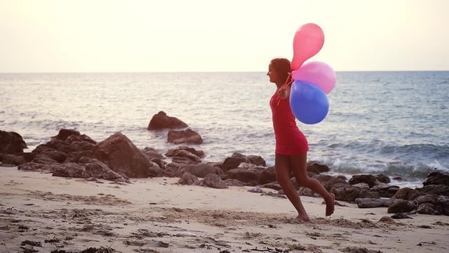 Happy young beautiful woman with balloons in hand running on the beach in slow motion. Concept about birthday and happy events. 1920x1080