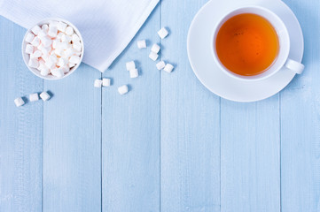 Background with cup of tea and marshmallow on the light blue wooden table