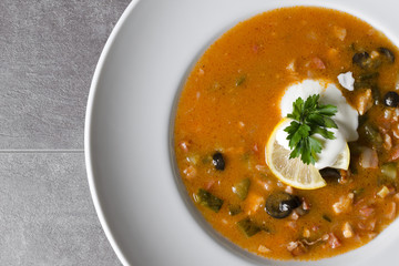 Hearty meat soup in a white plate with lemon and sour cream