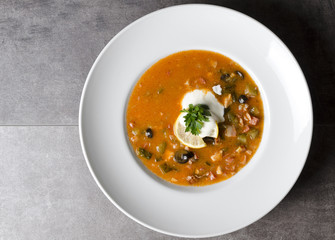Hearty meat soup in a white plate with lemon and sour cream