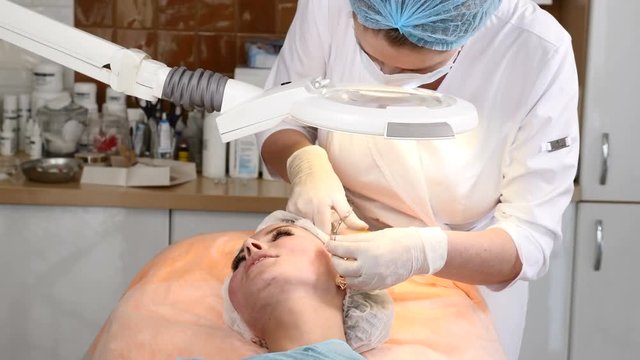 Healtcare clinic. Young female client gets thread face lifting procedure. Beautician in gloves making face anti-aging to a female face