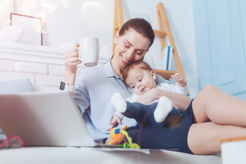 Happy motherhood. Cheerful pretty nice woman smiling and enjoying her tea while spending time with her daughter