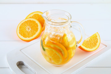 Orange detox water in a jug on a white wooden table. Healthy food, drinks.