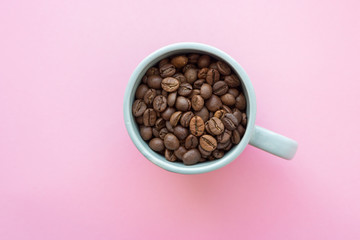 Coffee beans in blue cup on pink background view from above. Breakfast concept. Coffee seeds closeup. Morning with coffee drink. Cafe concept. 