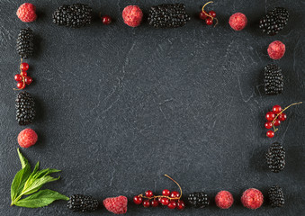 Frame made of red blackberries, raspberries and currant on a black surface.