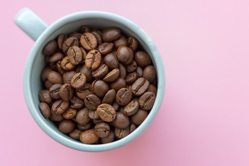 Coffee beans in blue cup on pink background view from above. Breakfast concept with copy space. Coffee seeds closeup. Morning with coffee drink. Cafe concept. 