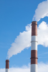 The steaming pipe of the plant or factory on the background of the blue sky.