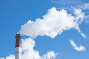 The steaming pipe of the plant or factory on the background of the blue sky.