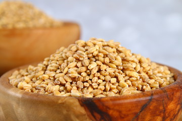 Dry pearl barley in a wooden bowl on a gray concrete table.