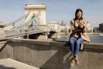 Young woman using mobile phone with Chain bridge at background in Budapest