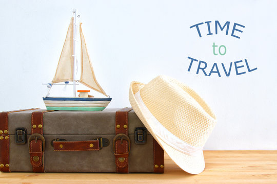 traveler vintage luggage, boat and fedora hat over wooden table. holiday and vacation concept.