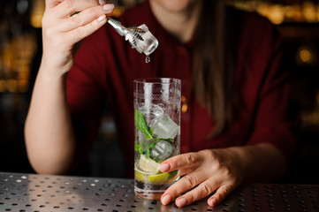 Female bartender adding an ice cube with tongs to the cocktail