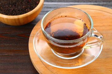 Hot black tea in a glass cup and dry tea on a wooden table.
