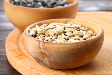 Black peeled and unpeeled sunflower seeds in a wooden bowl on a wooden table.