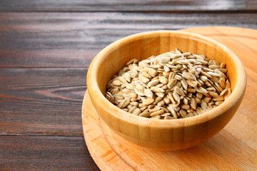 Black peeled sunflower seeds in a wooden bowl on a wooden table.