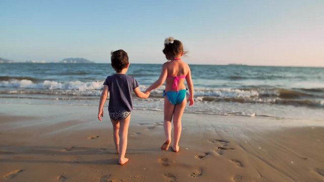 Boy and girl walking on the beach holding hands.