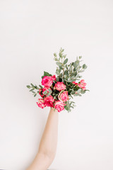 Female hand hold rose flowers and eucalyptus bouquet on white background. Flat lay, top view spring background.