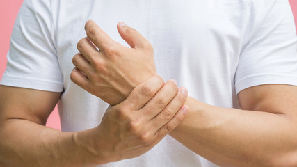Men feeling pain in his wrist on a pink background.