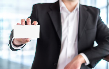 Casual business man holding empty white business card in modern office building. Free blank copy space.