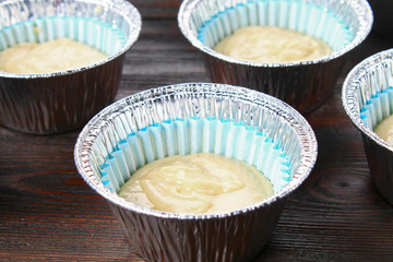 Dough in molds for muffins on a wooden table.