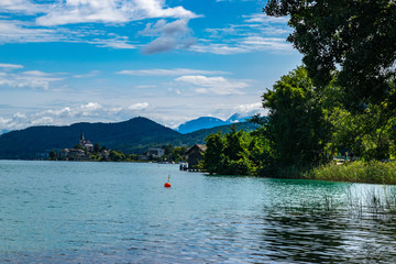 Austrian lakeside summer view from the forests' edge with mountains in the distance.