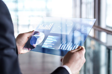 Transparent futuristic tablet. Business man using virtual touch screen. Modern mobile technology in accounting, finance, data and analytics. Internet of things (IOT) and augmented reality concept.