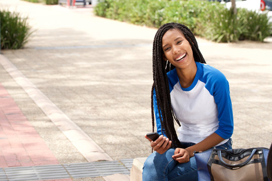 attractive young african woman sitting outside with smart phone and smiling