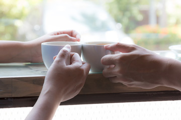 Two persons as couple drinking hot coffee together by sitting near window of cafe