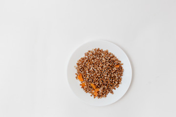 boiled buckwheat with carrot slices on white background, top view