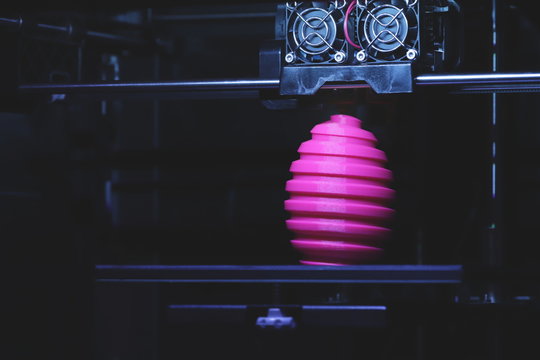 FDM 3D-printer manufacturing wound pink easter egg sculpture - front view on object and print head - dark technical look with selective light - background blanked out blurry