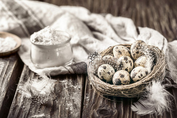 Fototapeta na wymiar Quail eggs in a nest and glass bowl of flour on a rustic wooden background.
