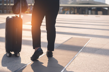 backside of beautiful traveler girl holding and pull luggage walking on concrete floor at outdoor in the city with sunlight and go to travel planing in vacation time concept.