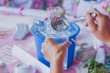 Close-up th hands add ice to the glass to distribute to friends