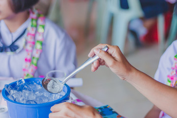 Close-up th hands add ice to the glass to distribute to friends