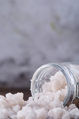 Spa concept. Bath salt pouring out of glass jar on wooden table, close-up, selective focus