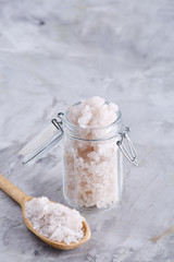 Spa concept. Bath salt pouring out of glass jar on texrured background, close-up, selective focus