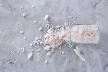 Spa concept. Bath salt pouring out of glass jar on texrured background, close-up, selective focus