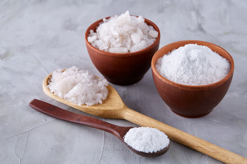 Conceptual composition of salt and pepper on spoons and bowls over light background, top view, close-up