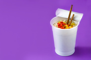 Take away noodles with vegetables on violet background. Copyspace