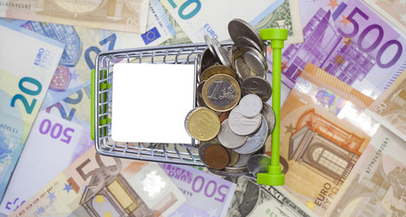 shopping cart with coins and banknotes in background. white board for list to buy in the frame
