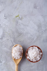 Composition of sea salt in ceramic bowl and spoon for cooking or spa on white background, top view, selective focus