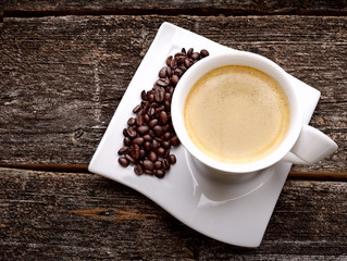 white cup of coffee with coffee beans on  wooden background