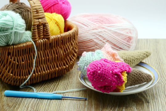 crochet ice cream cone in a sugar box with wool on table background. Basket with wool balls aside.