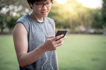Young Asian man runner listening to music from smartphone while running in the park. urban running with smart device concept