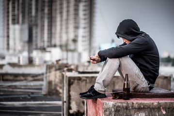 Mystery man in hoody jacket, sitting and hugs his knees up with an empty and broken bottle. depression self destruction suicidal addicts drug, Major depressive disorder concept - obrazy, fototapety, plakaty