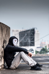 Fototapeta na wymiar Mystery man in white mask with hoody jacket, sitting thinking of something with sad eyes. depression self destruction suicidal addicts drug concept