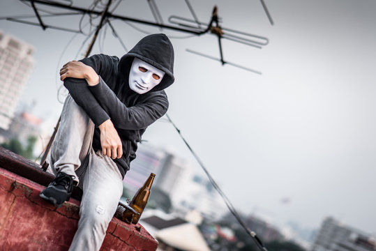 Mystery man in white mask with hoody jacket, sitting and hugs his knees up with broken empty bottle. depression self destruction and alcoholism. Major depressive disorder concept